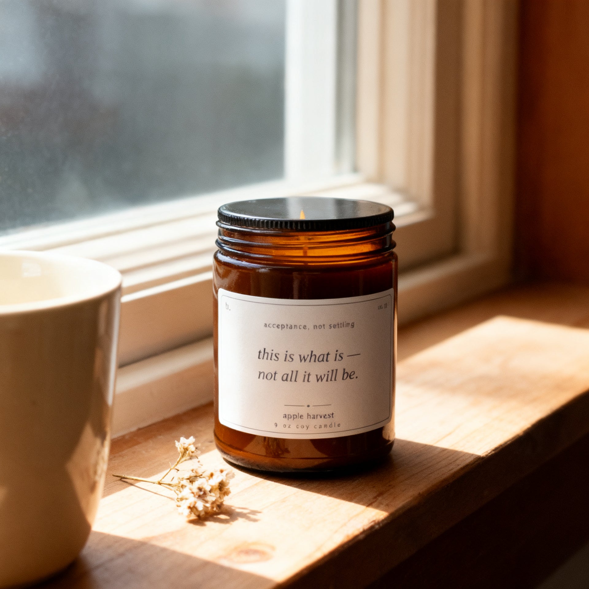 b.here apple harvest candle on a sunlit windowsill with a ceramic mug and dried flowers